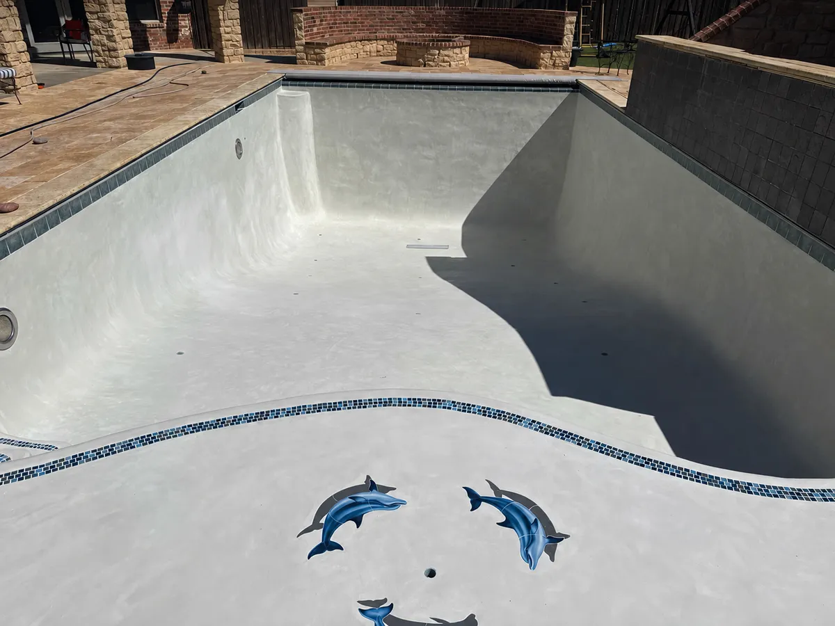 After: Drained pool with a light finish and dolphin designs beside a stone patio